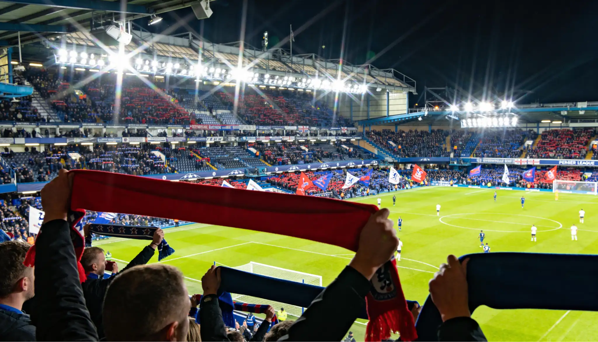 Estadio de la Premier League iluminado durante partido nocturno con aficionados